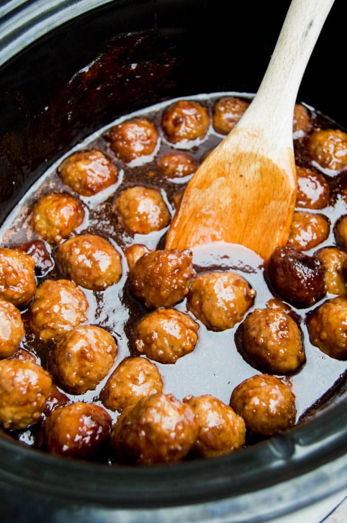 3 Ingredient Meatballs in a slow cooker with a wooden spoon.