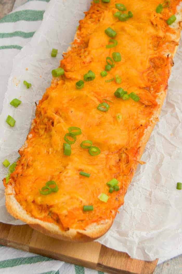 Buffalo Chicken French Bread Pizza on wooden board and white parchment paper topped with green onions