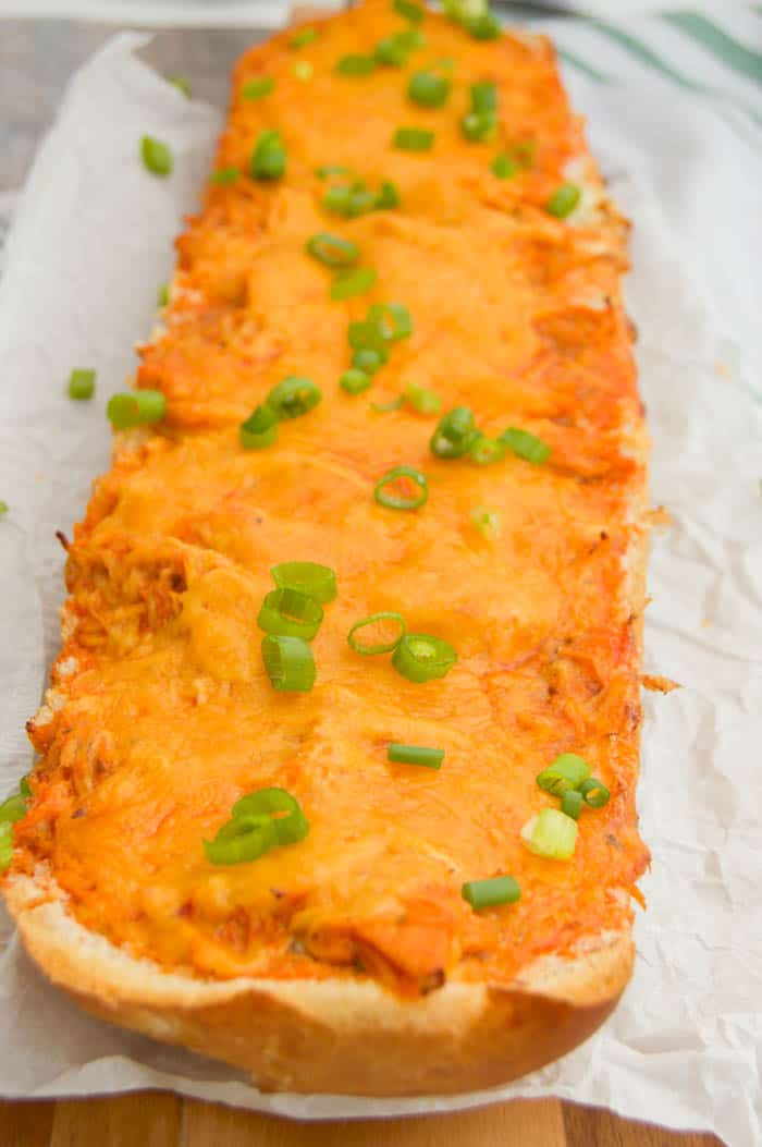 Buffalo Chicken French Bread Pizza on wooden board and white parchment paper topped with green onions