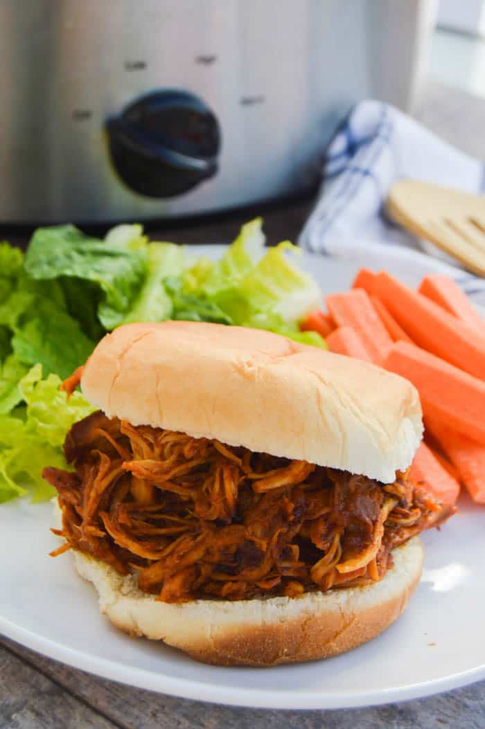 slow cooker root beer chicken on white plate with salad in the background