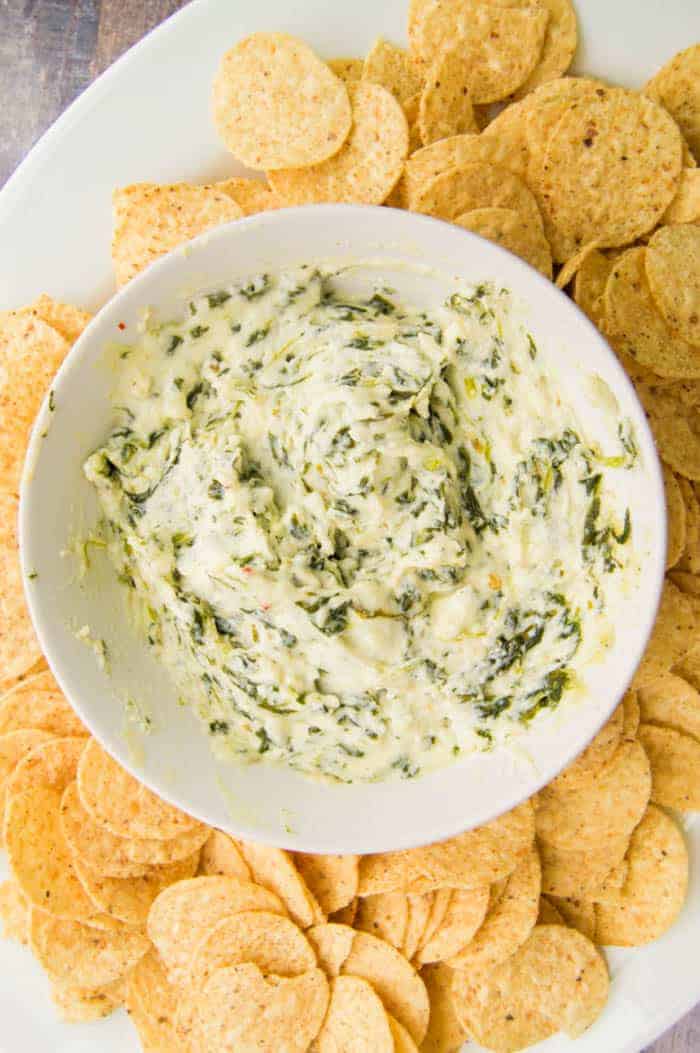 Cheesy Spinach Dip in white bowl on white serving tray surrounded by tortilla chips