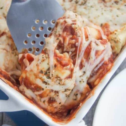 Ravioli Lasagna in white casserole dish being scooped by spatula