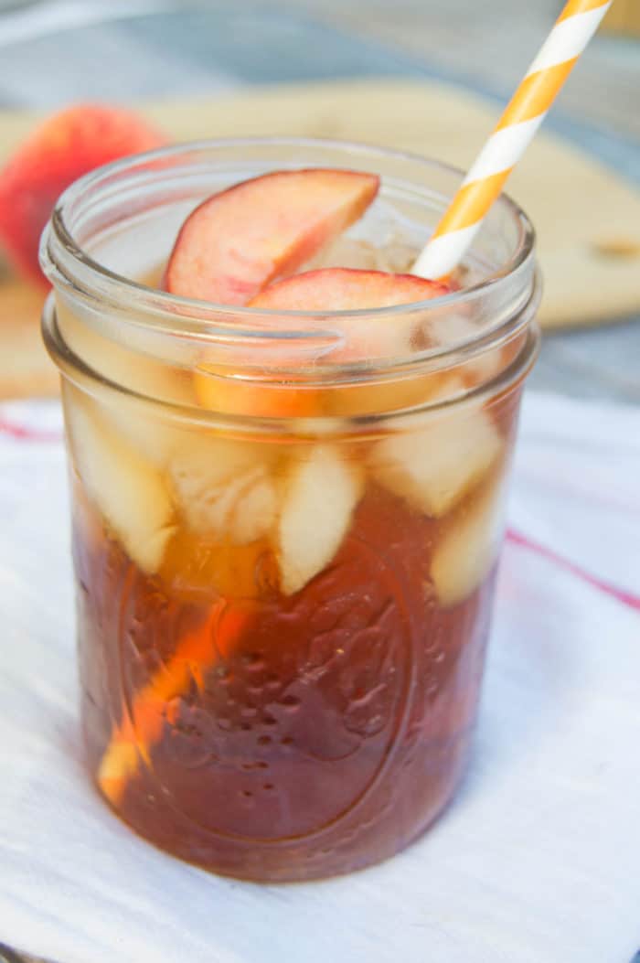 Peach Sweet Tea close up in Mason Jar with straw and sliced peaches on top.