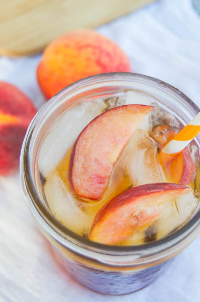 Peach Sweet Tea close up in mason jar with peaches behind it.