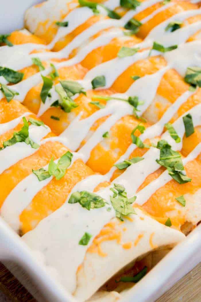 Closeup shot of Cheesy Ranch Chicken Enchiladas in white backing dish