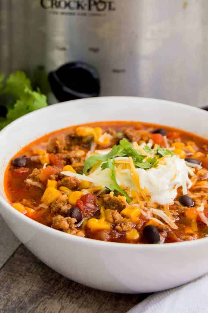 Slow Cooker Taco Soup in white bowl with slow cooker in the background.