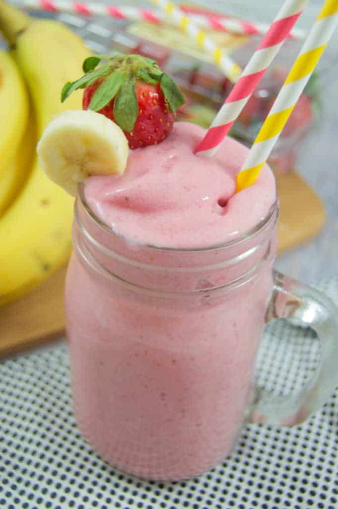 Strawberry Banana Smoothie in glass with 2 straws and bananas in the background