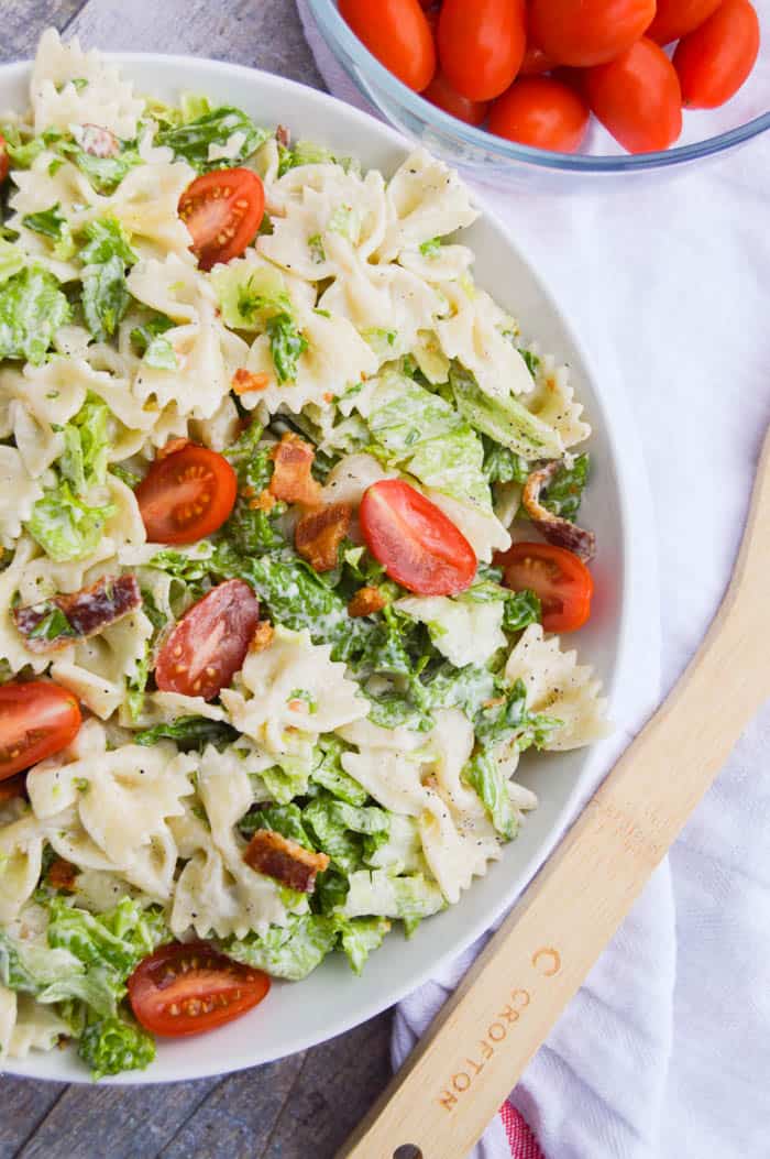 BLT Pasta Salad in a white bowl with wooden spoon and tomatoes.