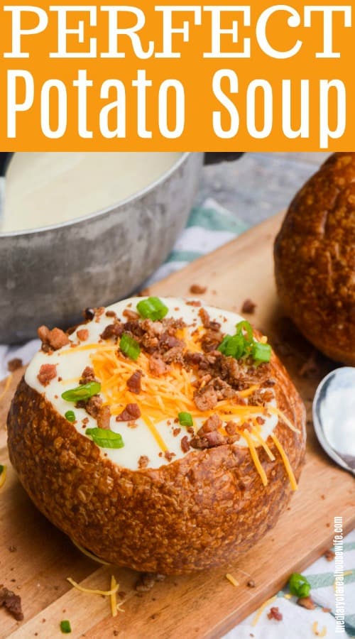 Potato soup in a bread bowl, topped with cheese. bacon bits, and chives on a wooden board with the title