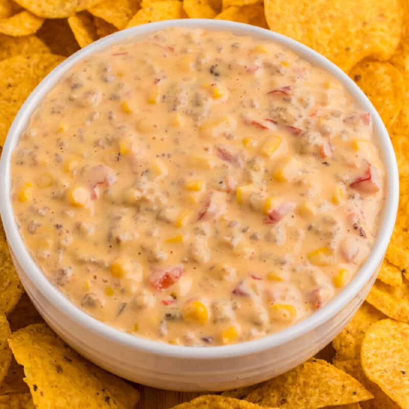 sausage dip in a white bowl with chips all around it
