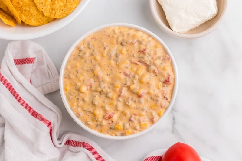 sausage rotel dip served in a white bowl with chips, tomatoes, and cream cheese on the side.