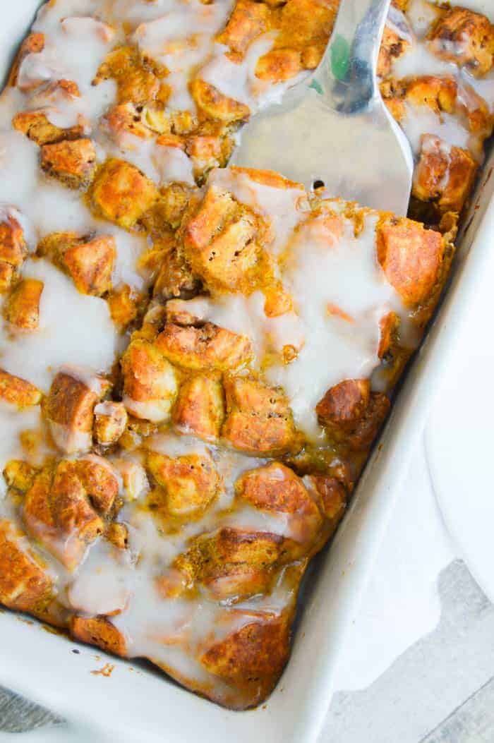 Pumpkin Cinnamon Roll Casserole being served out of a white casserole dish