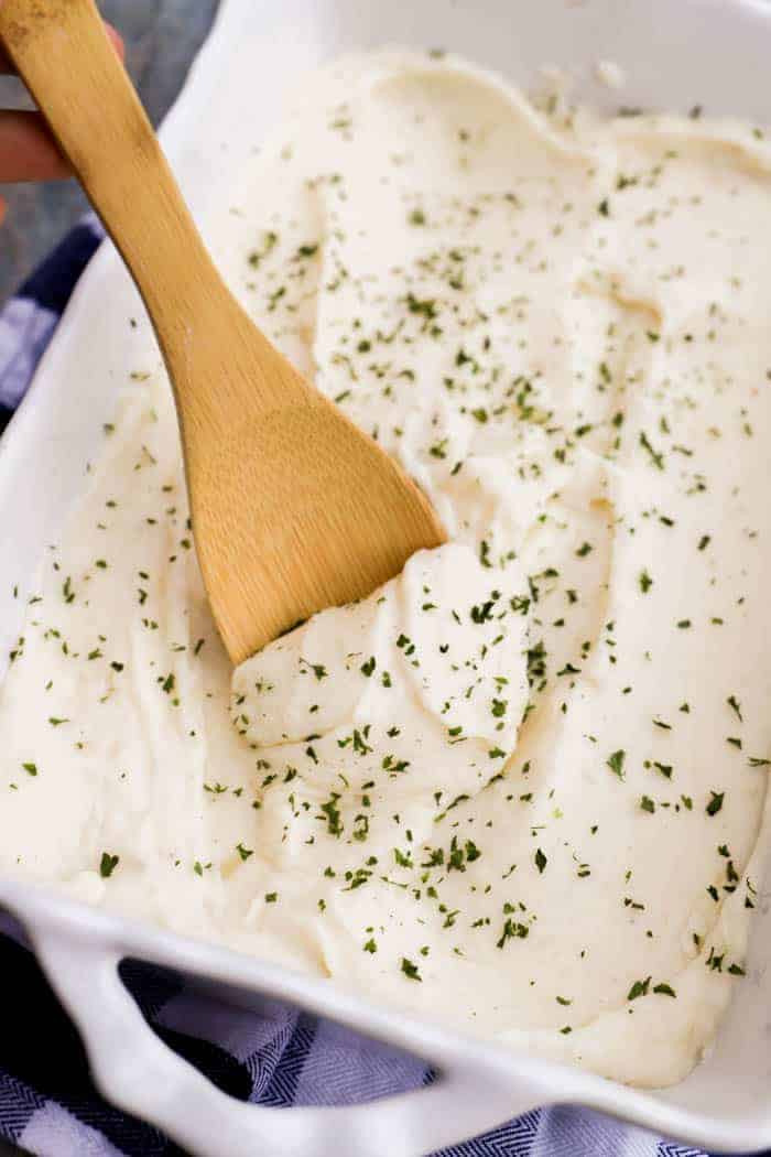 Make Ahead Mashed Potatoes in white casserole dish scooped out by wooden spoon