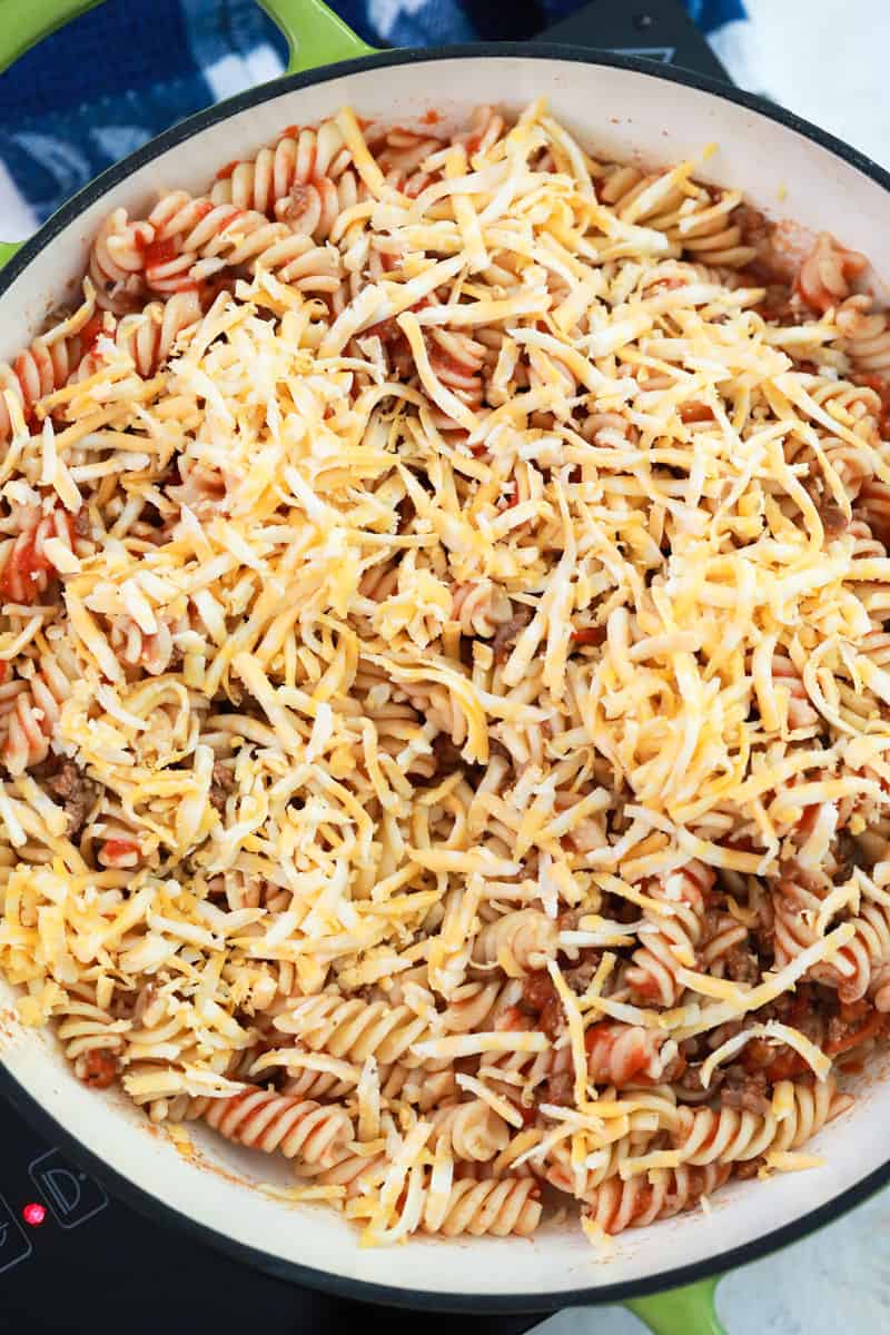 topping the cheesy taco pasta with shredded cheese