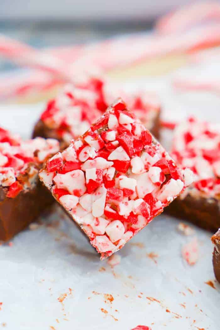 Fudge on a parchment paper with candy canes in back