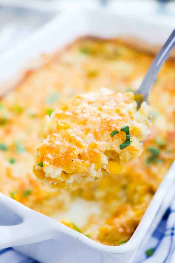 Corn Pudding in white casserole dish scooped out on spoon