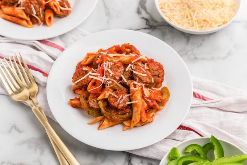 One-Pan Italian Sausage and Peppers Penne on a white plate with rose gold forks on the side