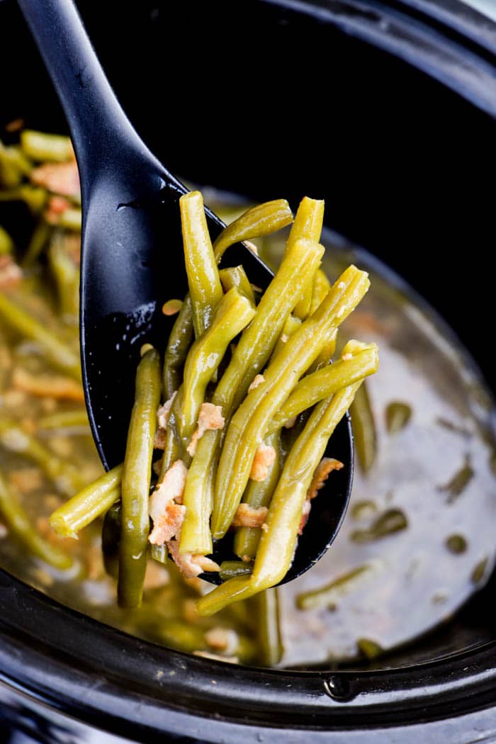 Slow Cooker green beans out of the crockpot on a black spoon