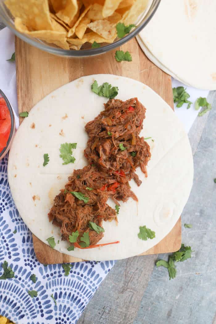 4 Ingredient Slow Cooker Steak Fajita on the table with chips and tomatoes