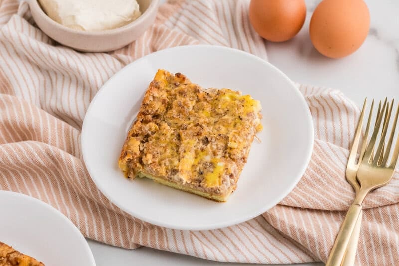 Cream Cheese Sausage Casserole on a plate in kitchen with eggs and cream cheese.