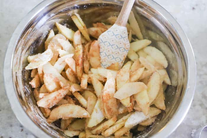 mixing apples in a silver mixing bowl