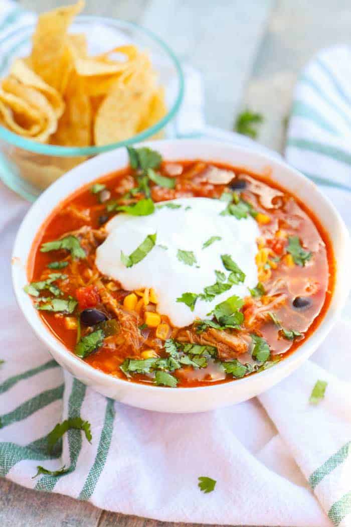 Pulled Pork Taco Soup in a white bowl with chips in the background