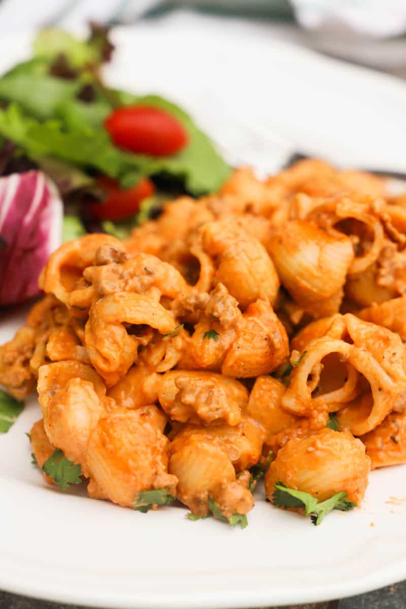 Creamy Ground Beef and Shells on a white plate with salad