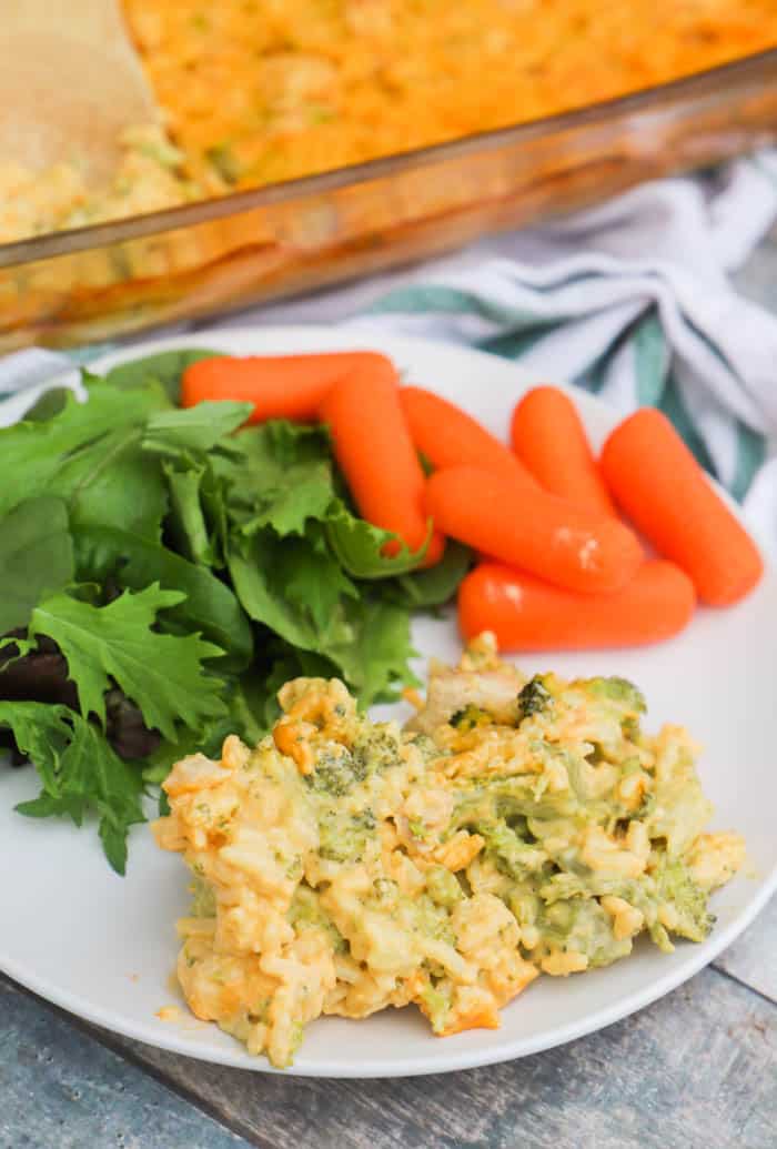 serving Cheesy Broccoli Chicken and Rice Casserole on a white plate with salad