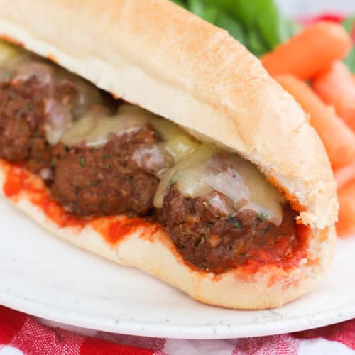 Meatball Subs on a white plate with salad and carrots