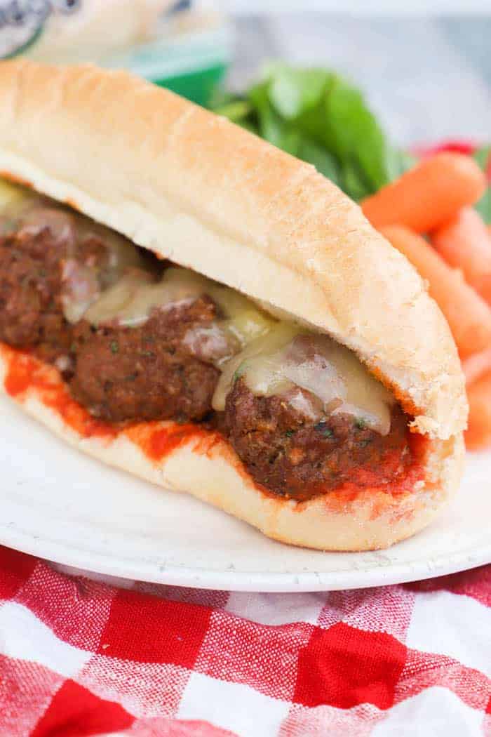 Meatball Subs on a white plate with salad and carrots