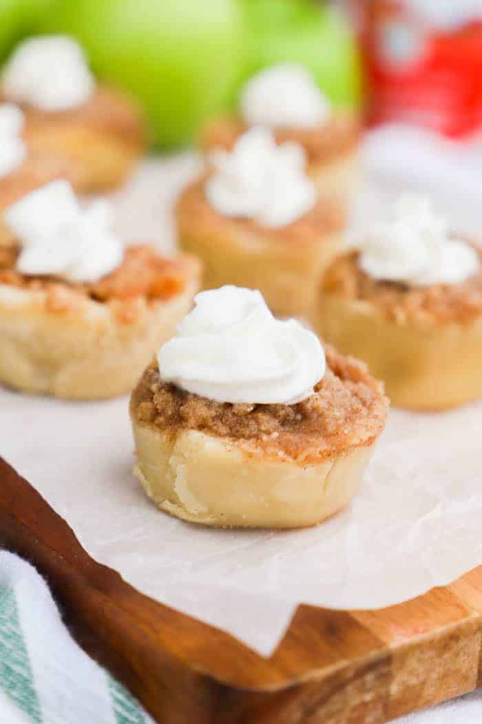 Mini Muffin Tin Apple Pies on white parchment paper topped with whipped cream