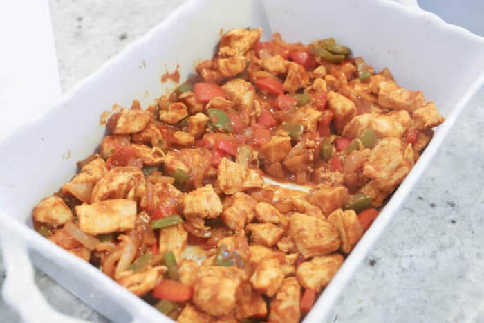 adding chicken and peppers to the bottom of a casserole dish