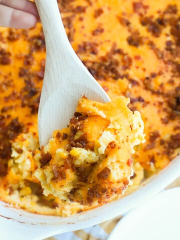 Bacon and Corn Casserole in a casserole dish on a wooden spoon