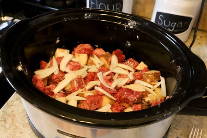 adding potatoes steak and onion to the slow cooker