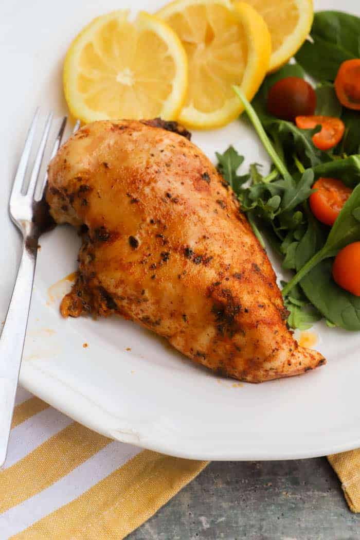 lemon pepper chicken on a plate with salad and slice lemons