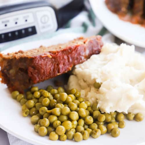 Slow Cooker Meatloaf on a plate with peas and mashed potatoes