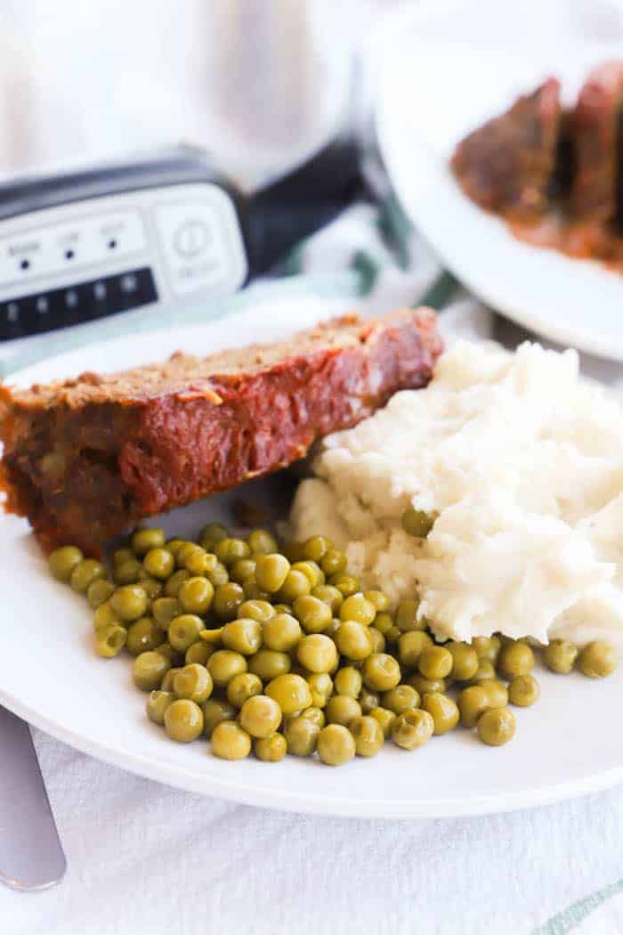 Slow Cooker Meatloaf on a plate with peas and mashed potatoes 