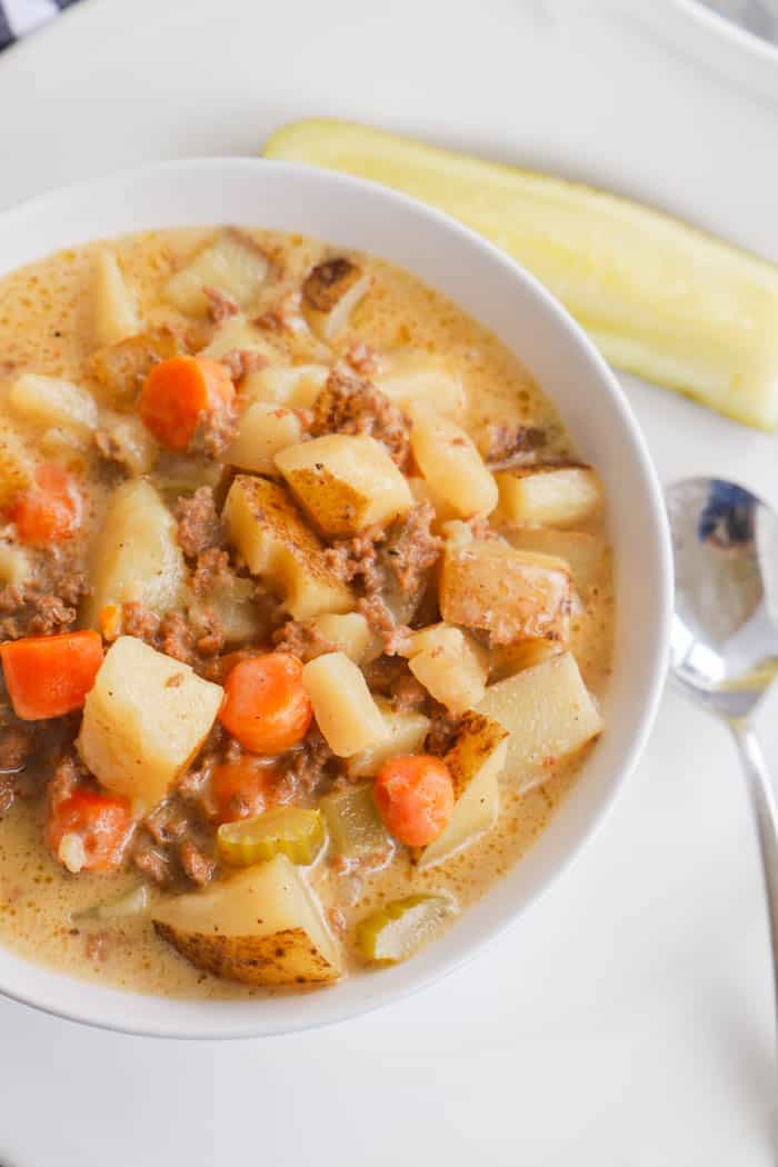 Slow Cooker Cheeseburger Soup in a white bowl with pickle on the side