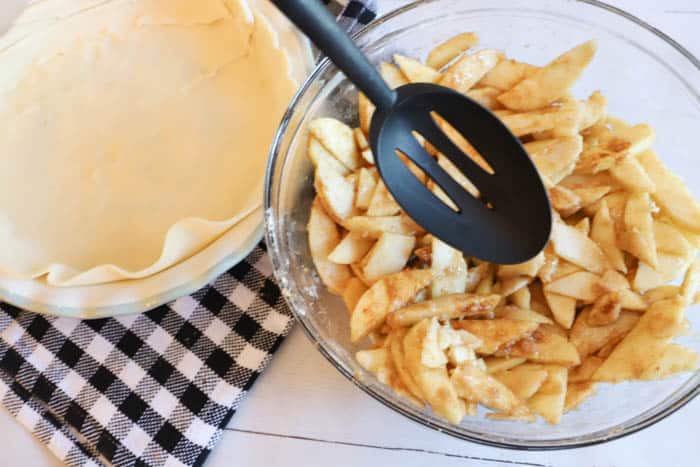 using a spoon to add apples to the pie crust