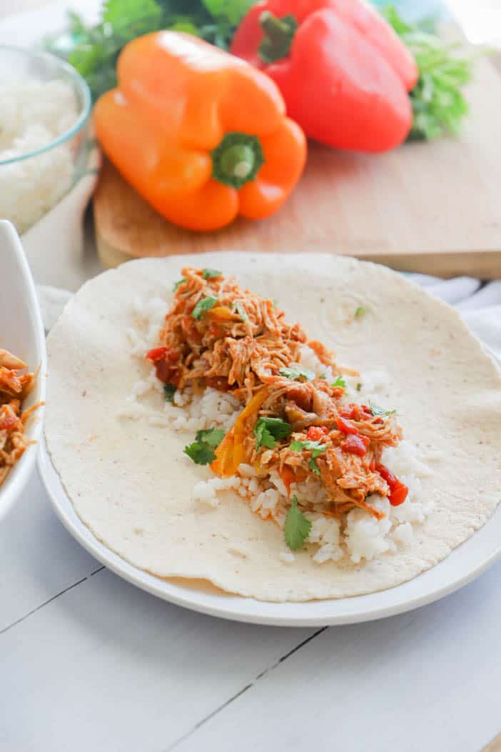Closeup shot of Chicken Fajitas over rice on a flour tortilla with bell peppers in background