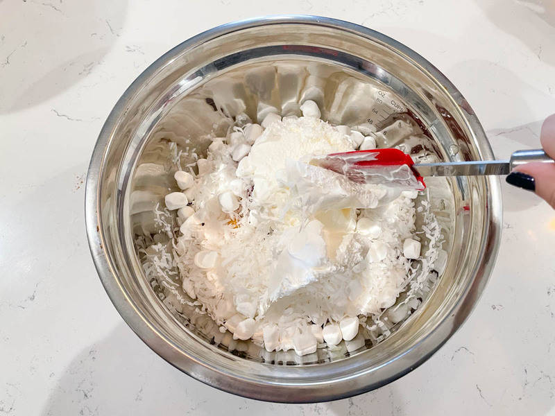 adding cool whip and sour cream to the ambrosia in a metal bowl