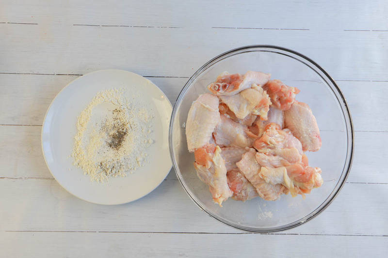 Chicken wings in a clear bowl with breading next to it.