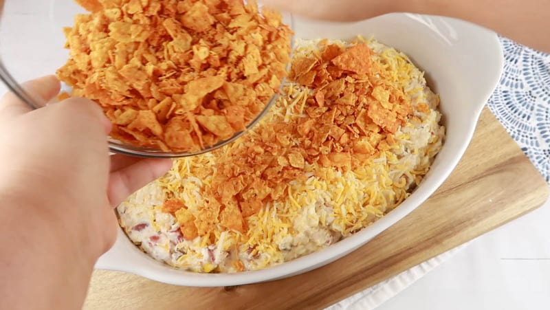 adding cheese and chips to the top of the casserole in white casserole dish