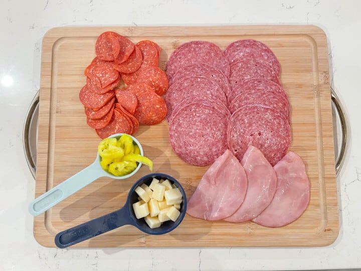 Meat and cheese for pasta salad on wooden board.