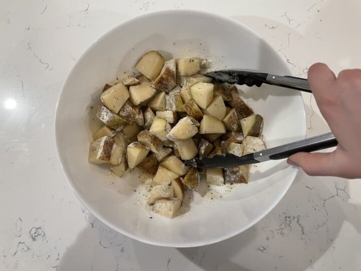 mixing potatoes oil and ranch seasoning in white bowl