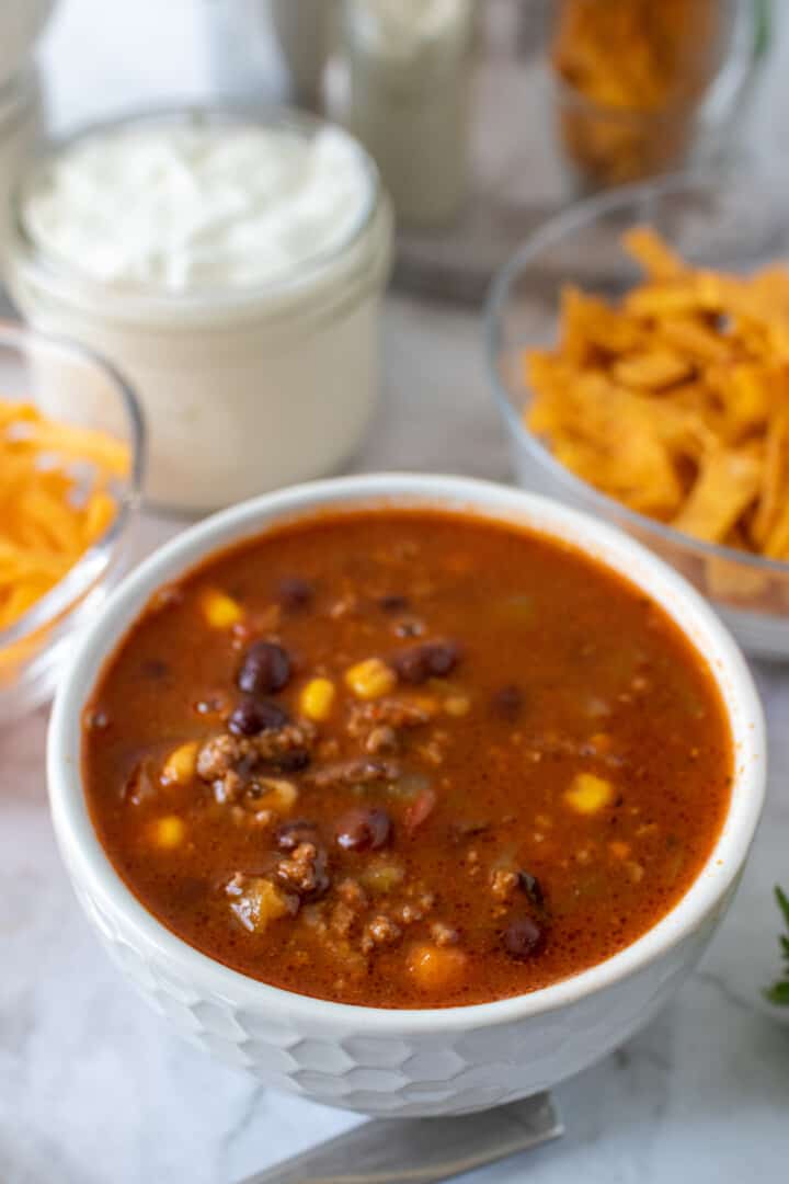 turkey taco soup in a white bowl with toppings in background