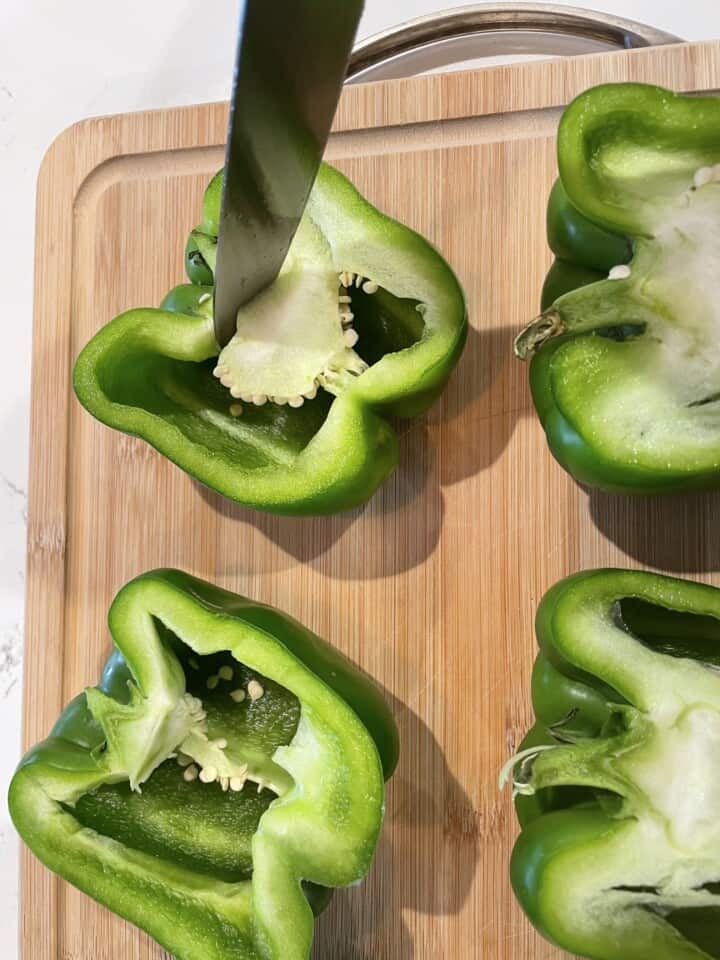 Halving and cleaning out bell peppers on a wood cutting board.