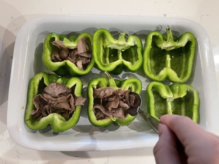 Adding roast beef to the bell peppers in white casserole dish.