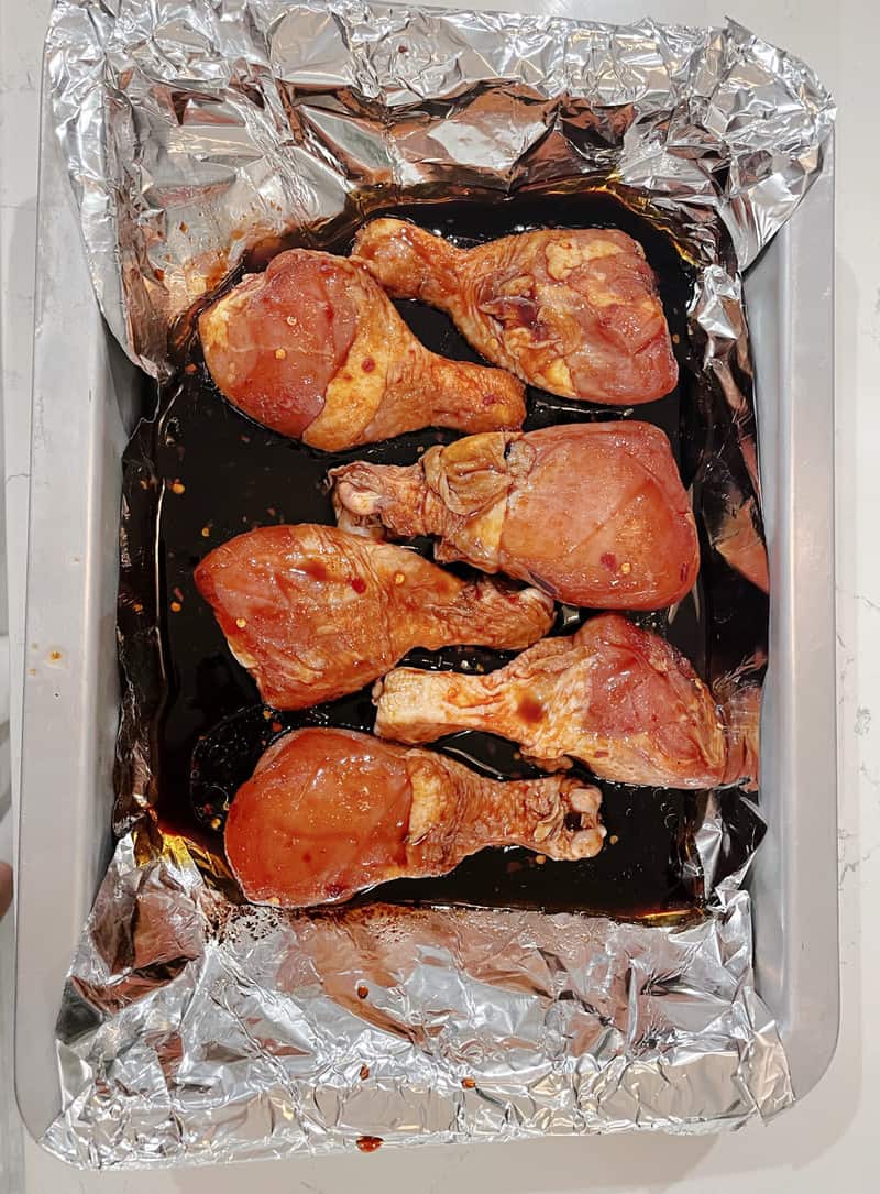 drumsticks in a baking pan with tin foil on the bottom and sauce poured in it.