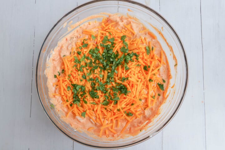 fiesta taco dip in clear bowl topped with cheddar cheese and cilantro